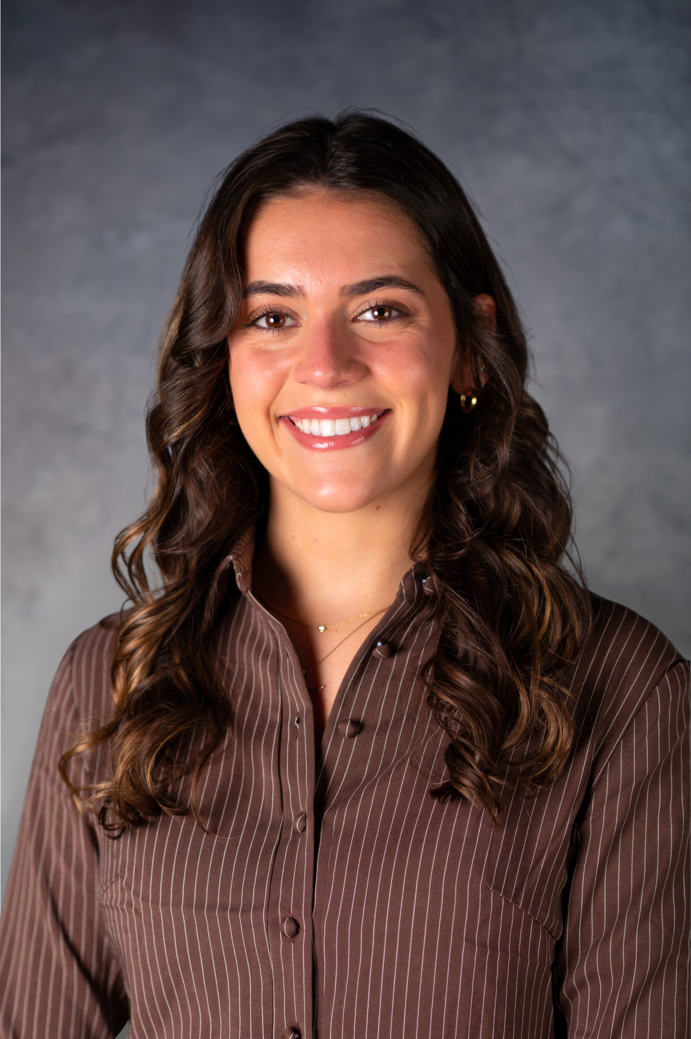 Woman with brown curly hair in a brown button down shirt smiling at the camera