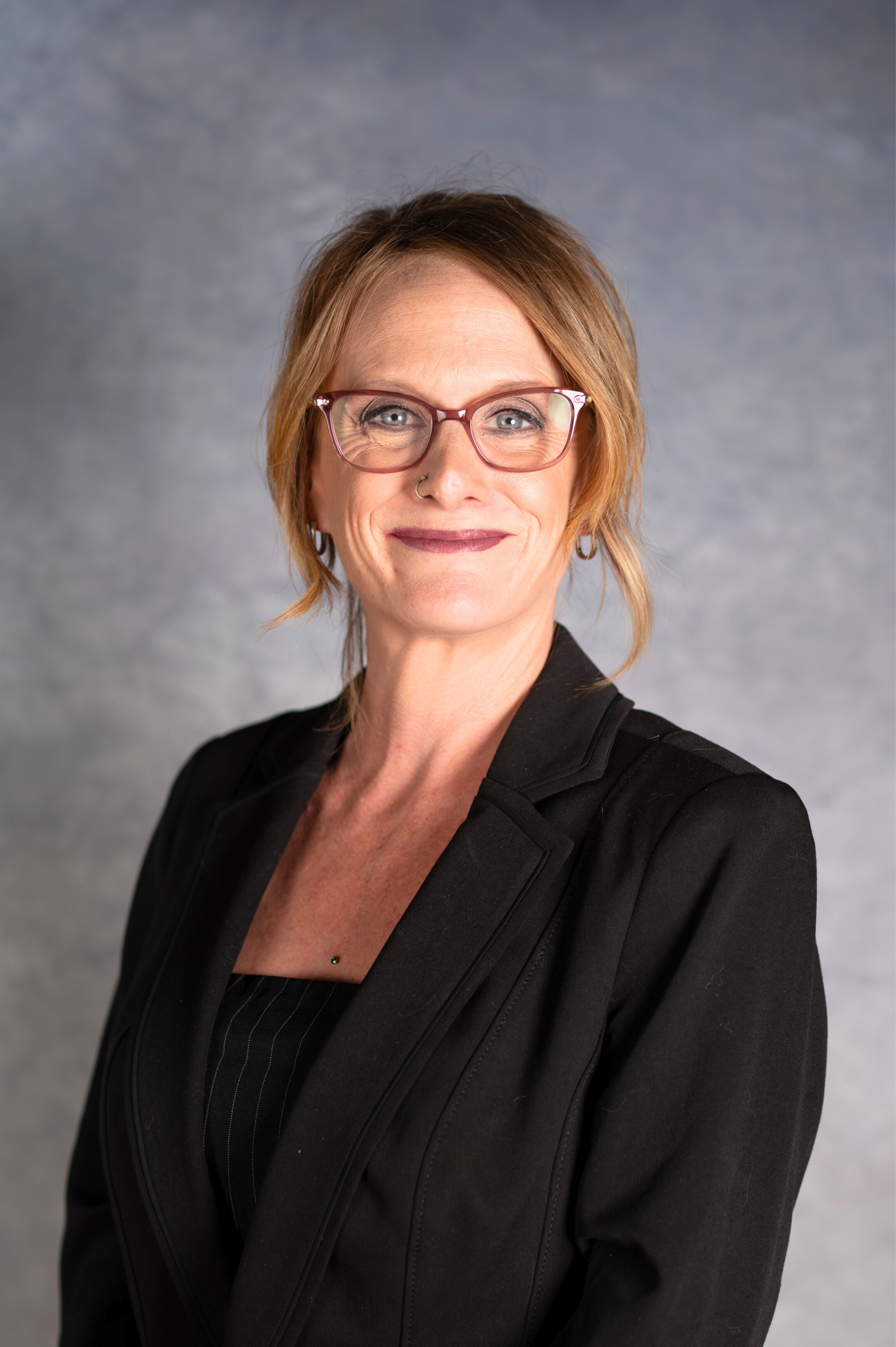 Woman smiling at camera in black blazer with hair pulled back.