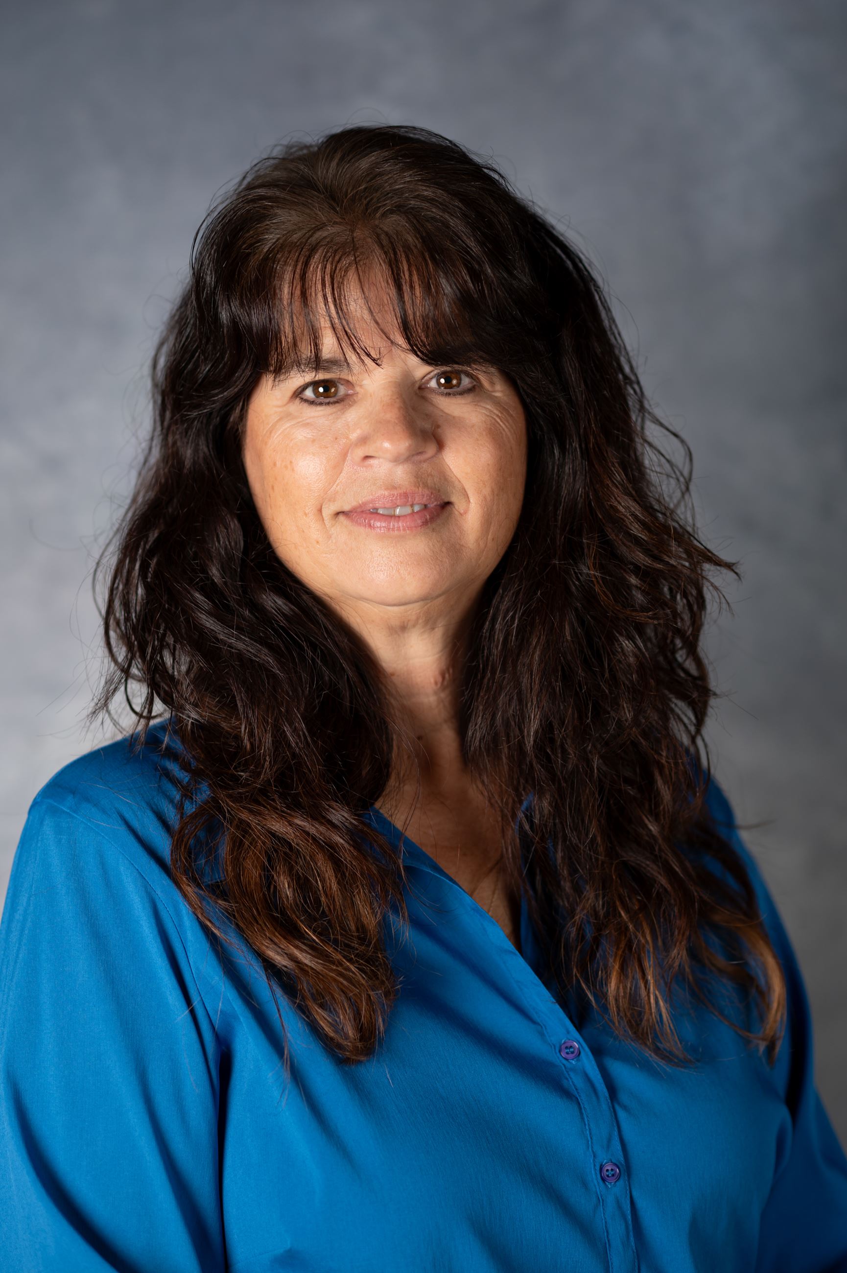 Woman with brown curly hair smiling at camera in blue blouse