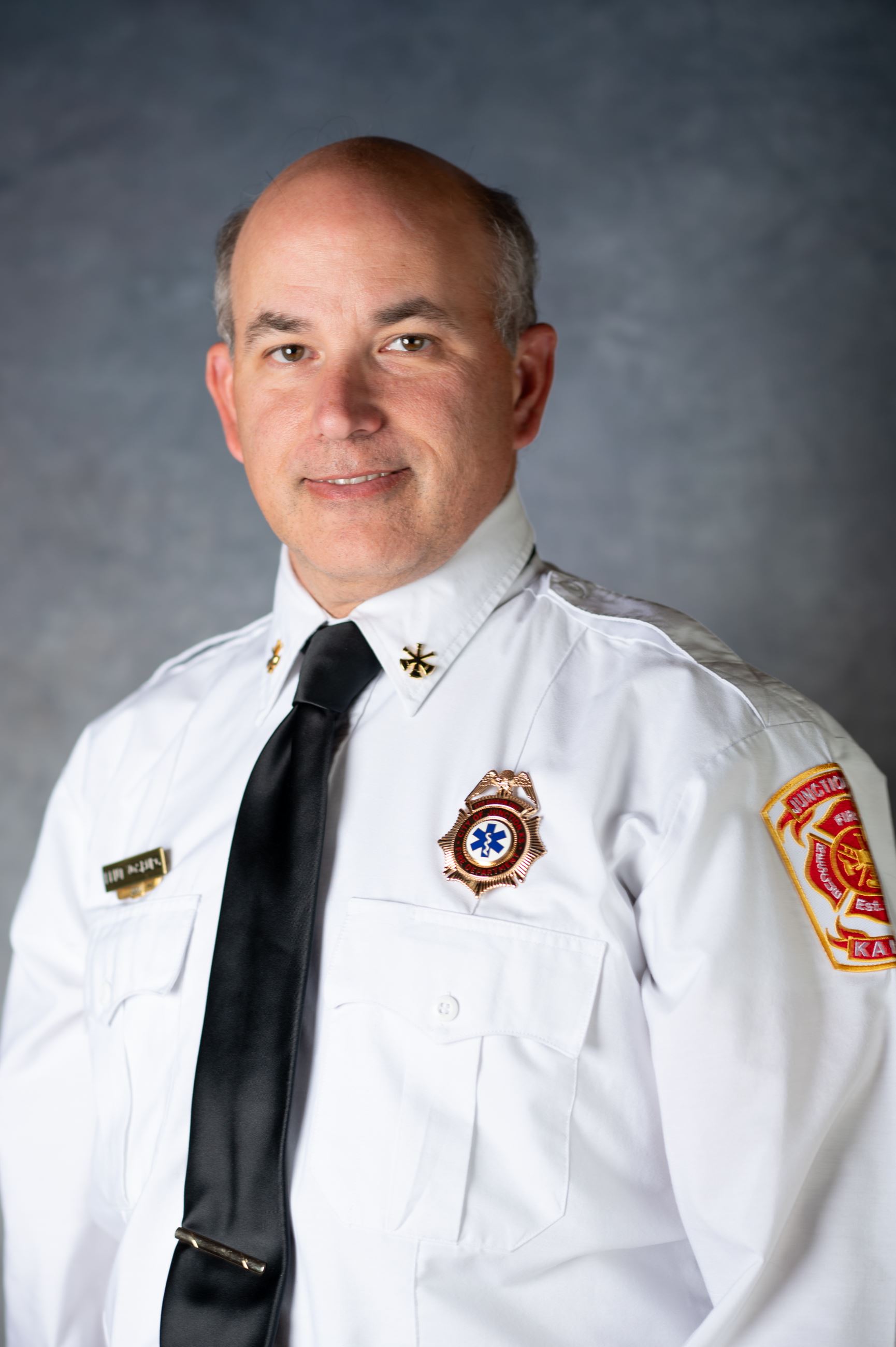 Older man wearing fireman's dress uniform smiles at camera