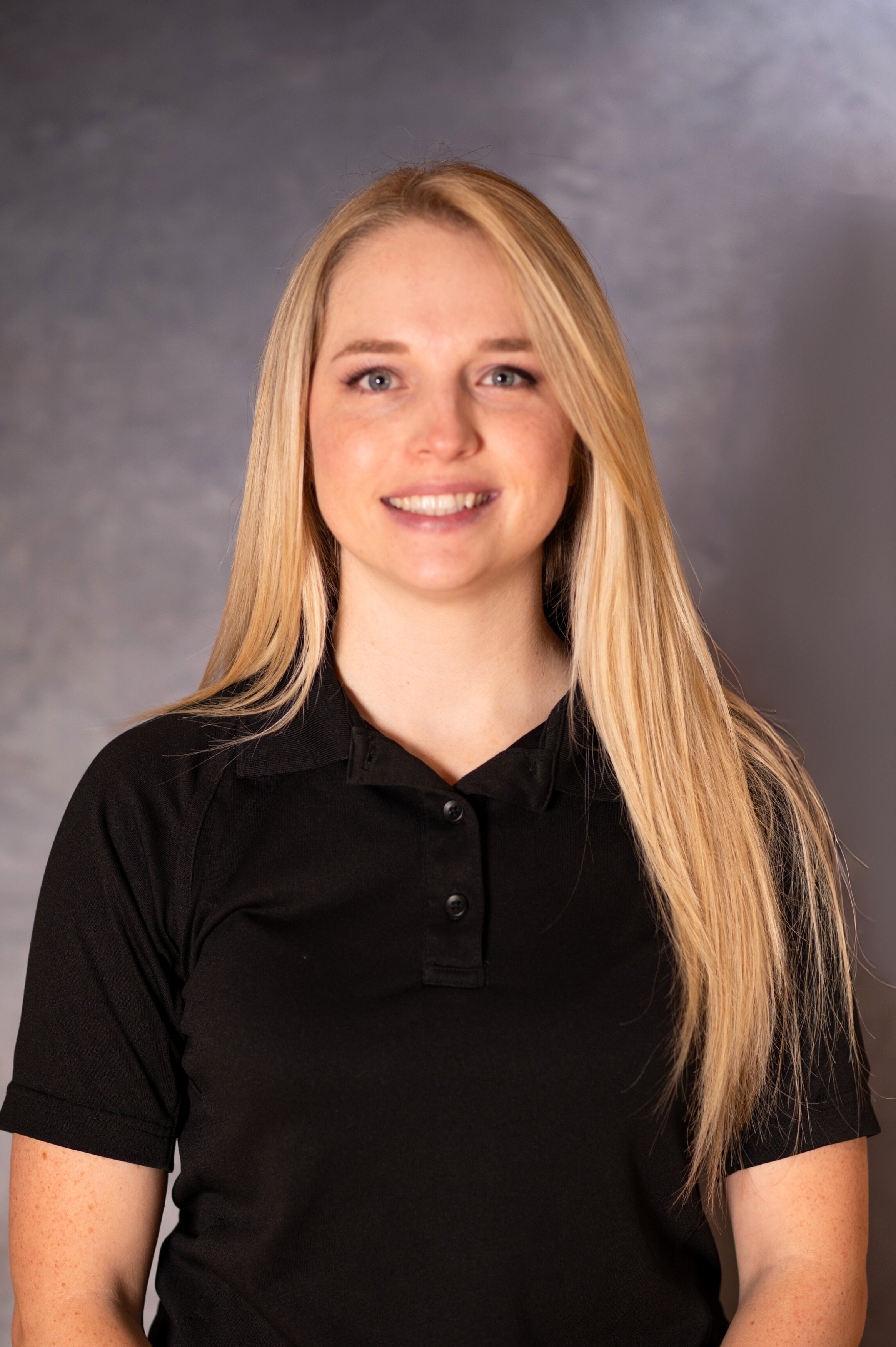 Young blonde woman in black button up smiles directly at camera