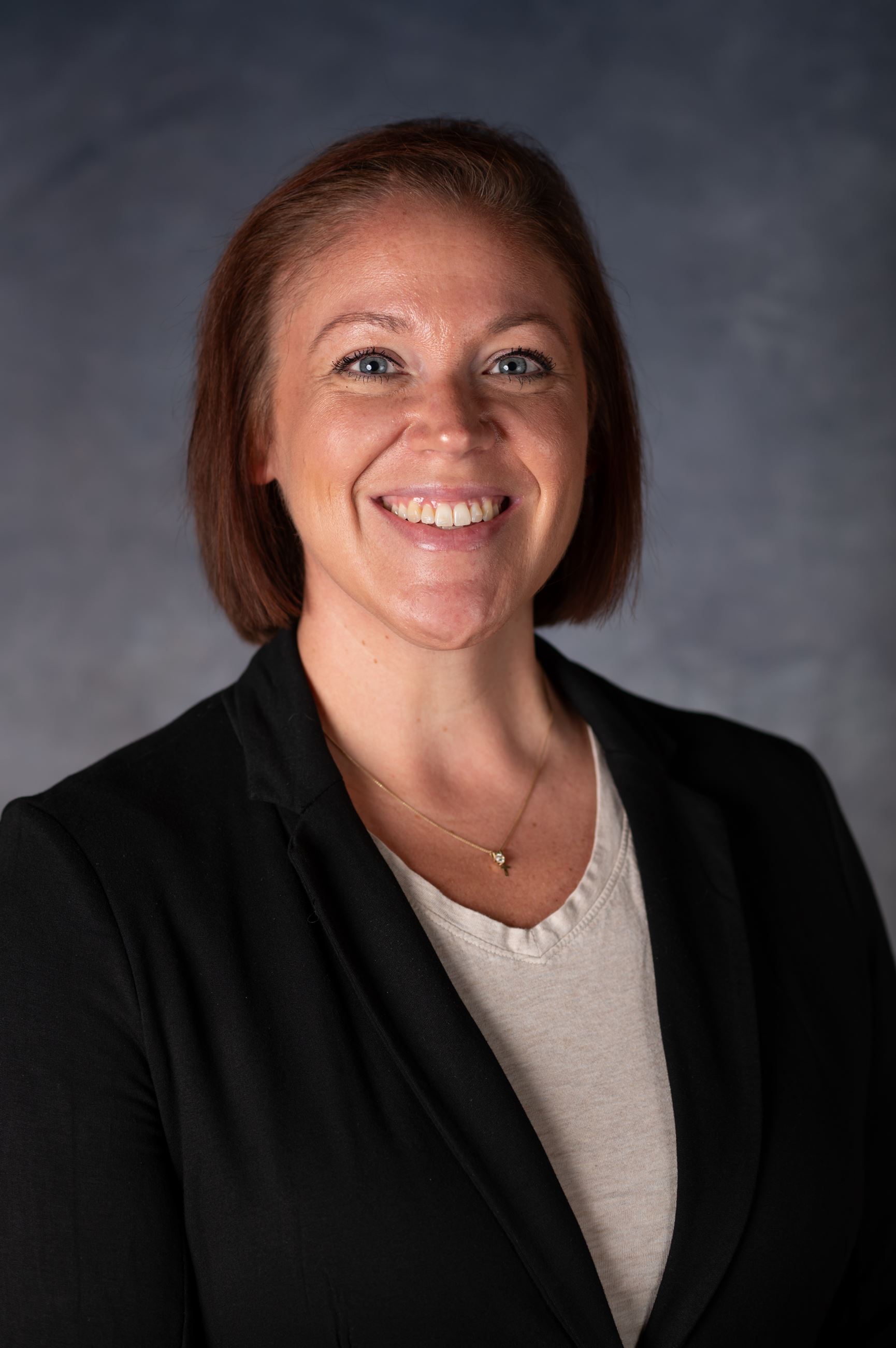 Woman with short brown hair wearing black blazer smiles directly at camera