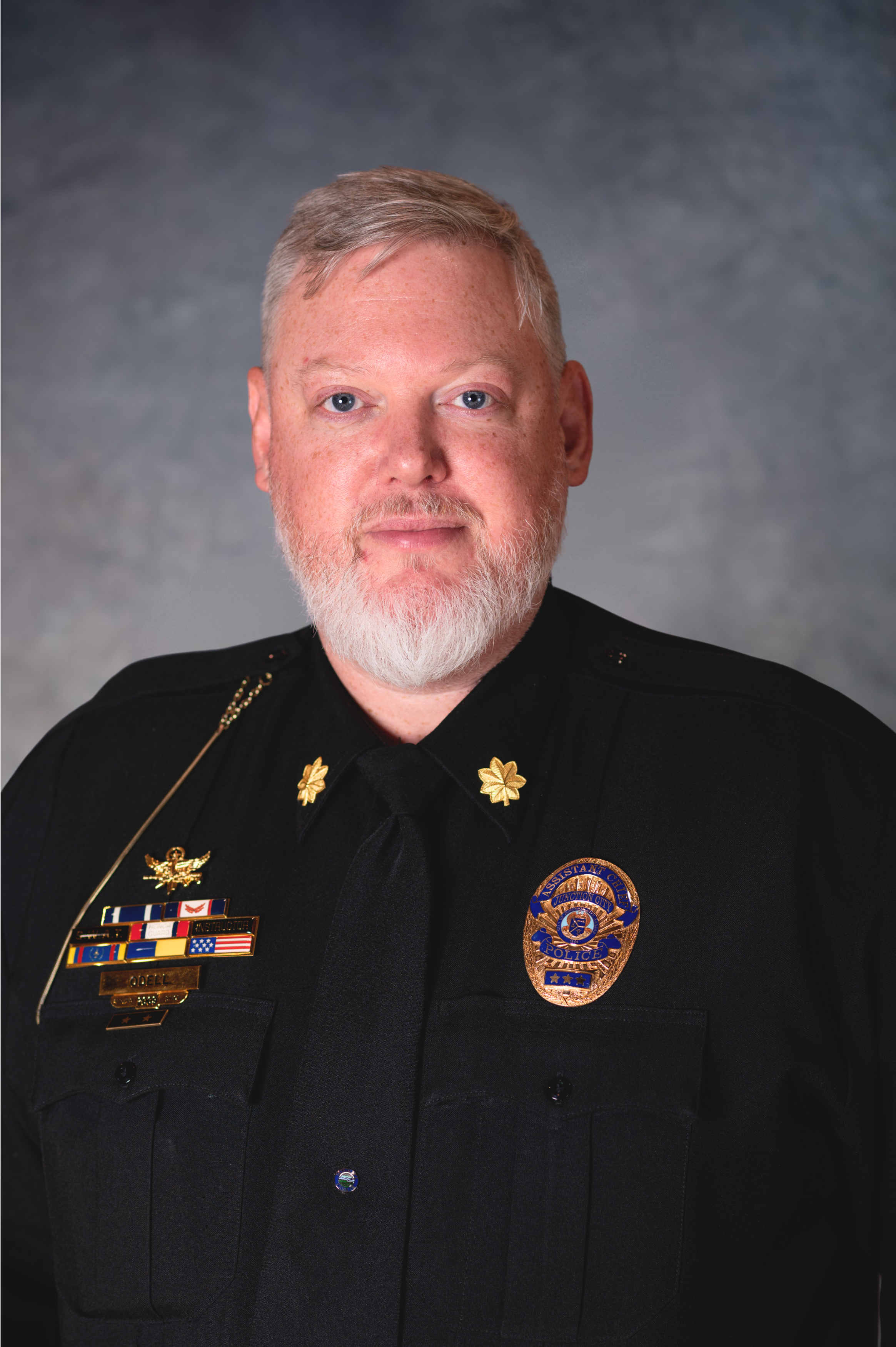 Middle aged man with white hair and freckles looks directly at camera wearing police dress uniform