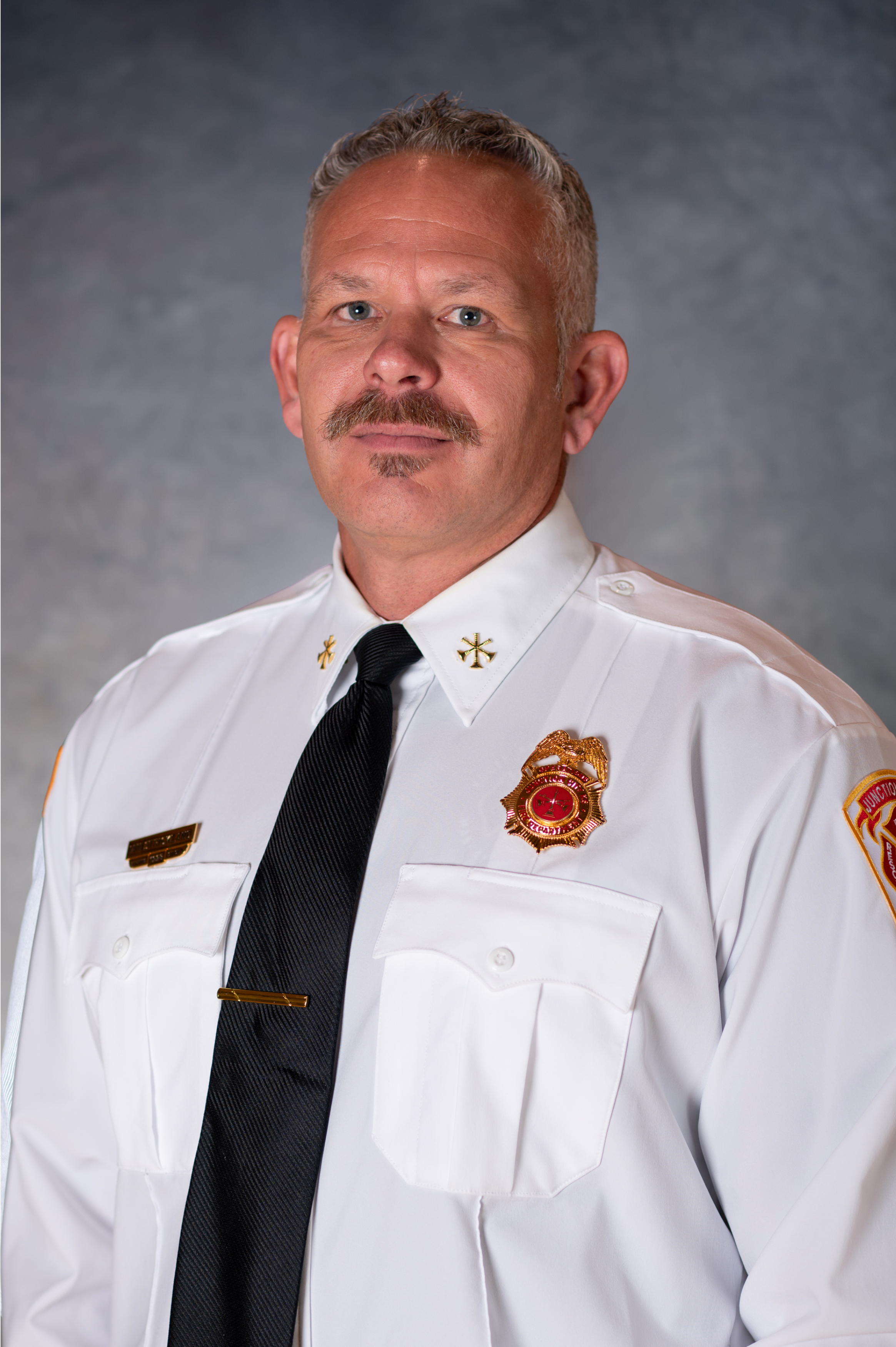 Man with salt and pepper hair with mustache wearing fireman's dress uniform