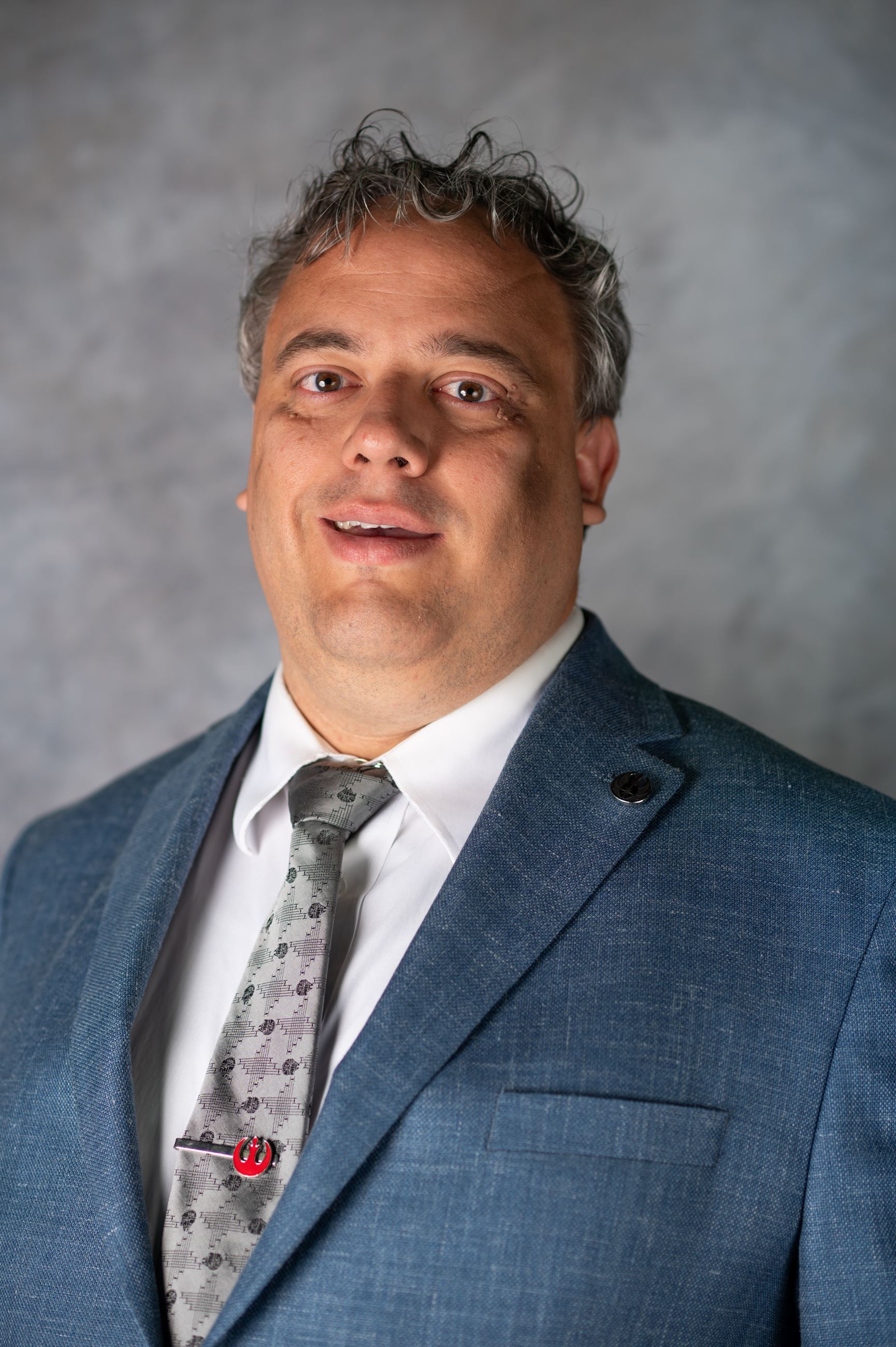Man in a blue suit and gray tie smiles directly at camera.
